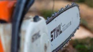 Close-up of a STIHL chainsaw bar and chain with orange body, cutting into wood.