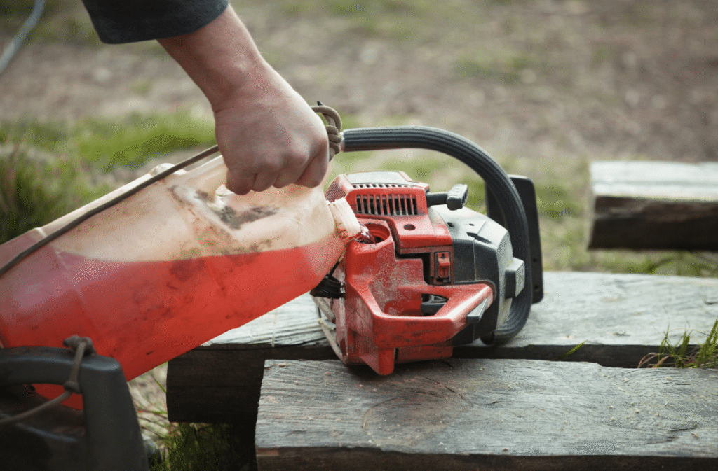 Person gripping a red chainsaw perched on a wooden beam outdoors, ready to cut wood outdoors at a worksite.